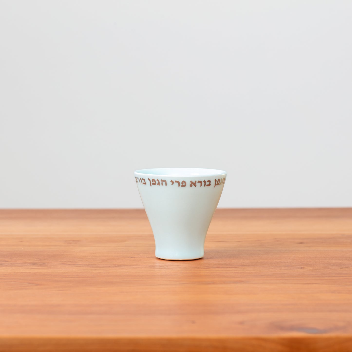 Sleek, traditional porcelain Kiddush Cup with gold lettering in Hebrew inscribed along the outer rim reading "boreh p'ri hagafen"