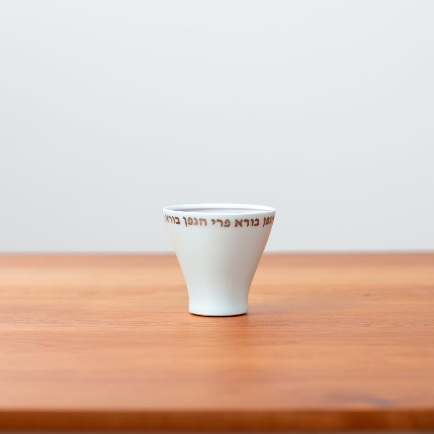 White porcelain Kiddush cup full of wine sitting on wooden table