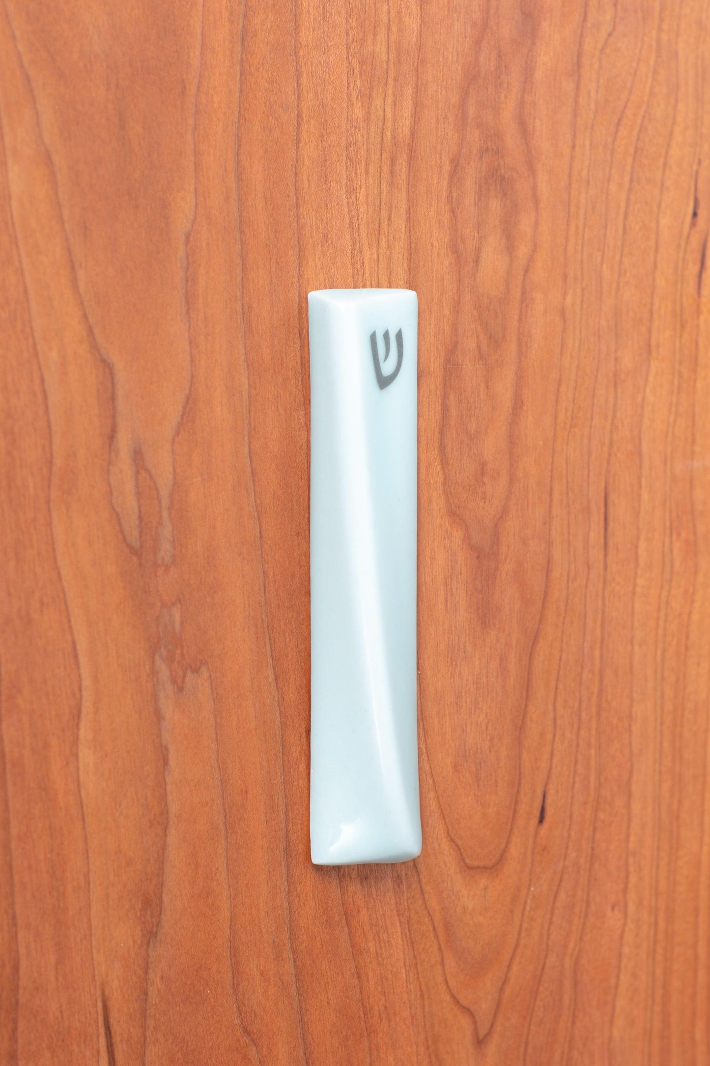 Handcrafted mezuzah affixed to a wooden surface, featuring a sleek, modern design with intricate detailing. A symbol of faith and protection, available at Green Judaica.